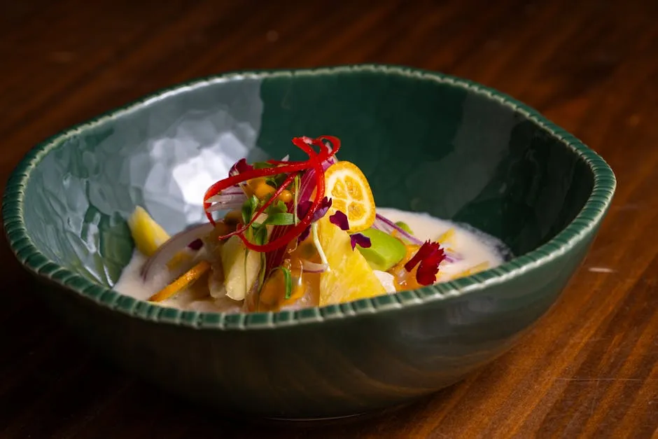 A colorful bowl of tropical fruits garnished with edible flowers and citrus in a green ceramic bowl.