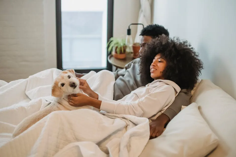 Young ethnic couple with dog lying in cozy bed covered with soft blanket at home