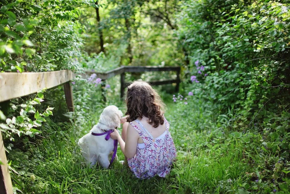 Girl and Puppy Sitting on Green Grass Surrounded With Plants During Daytime