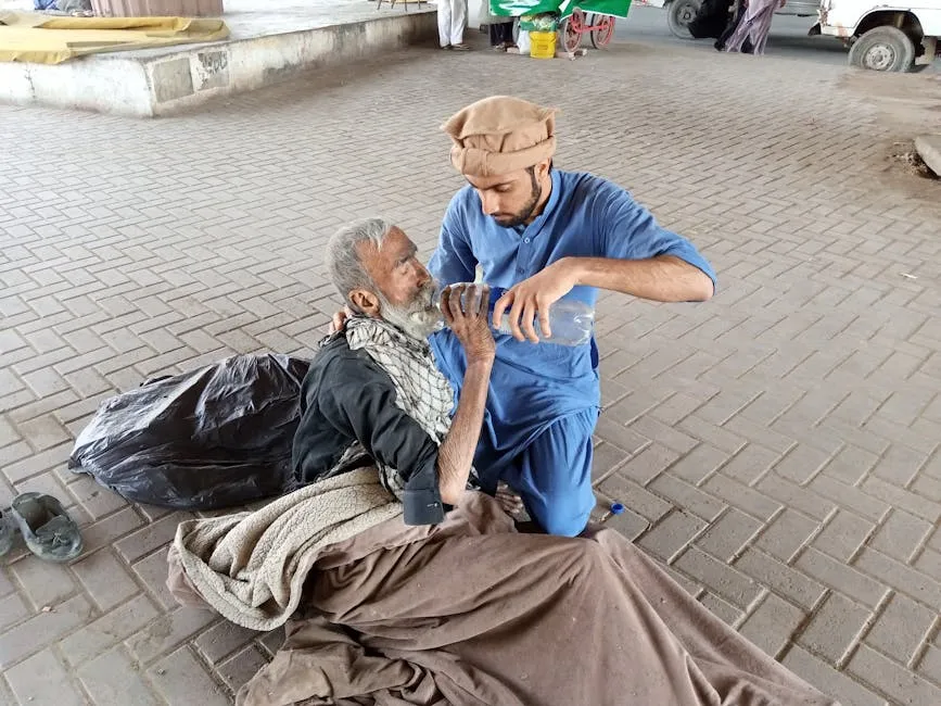 Man In Blue Clothing Giving An Old Man Water