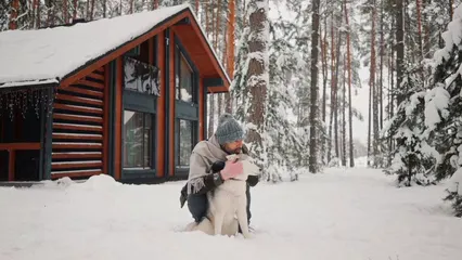 Horizontal video: A woman and her husky are sitting in the snow near a cabin 6497979. Duration: 21 seconds. Resolution: 1920x1080