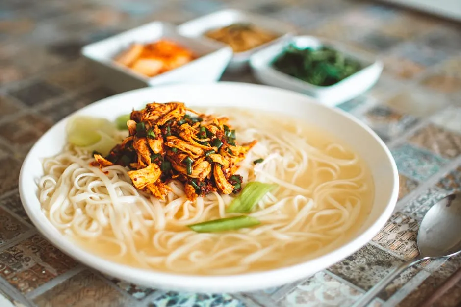 Delicious spicy chicken noodle soup served with lime and spices in a ceramic bowl.