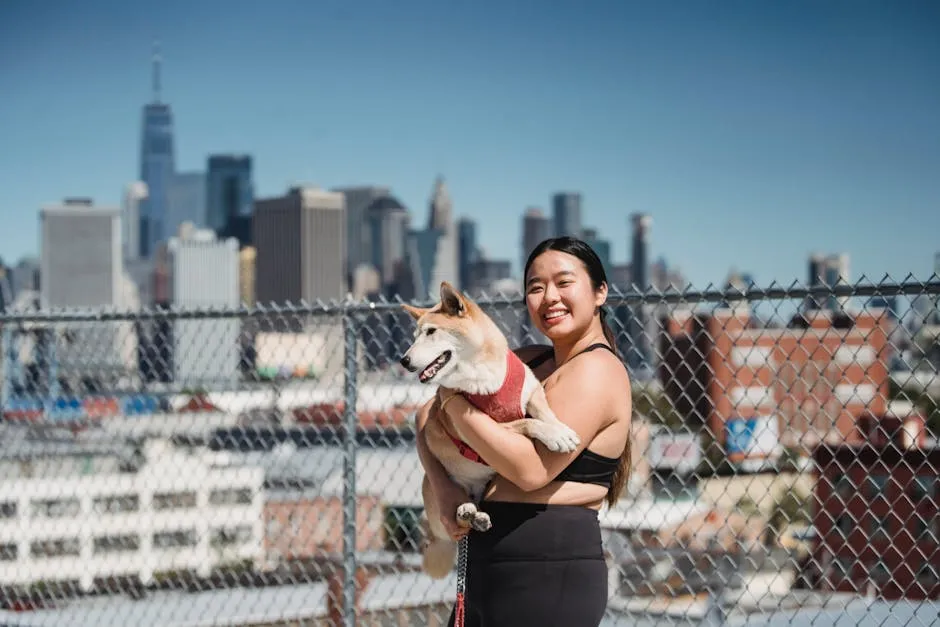 Cheerful Asian female in sportswear carrying cute puppy while walking together near city and looking at camera
