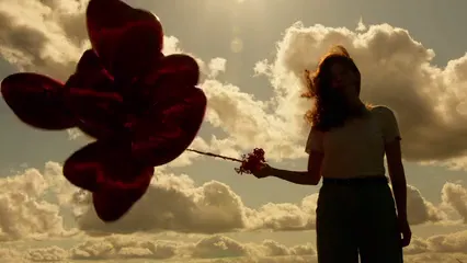 Horizontal video: Woman with bunch of heart shaped balloons standing against the sun 5457412. Duration: 14 seconds. Resolution: 3840x2160