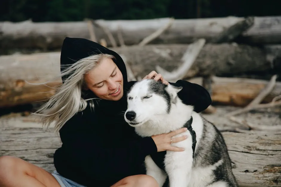 A woman in a hoodie petting her Siberian husky outdoors.