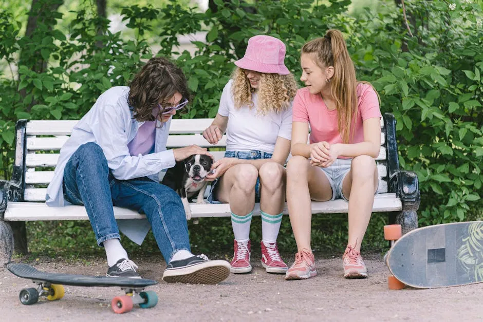 Three friends enjoy a moment with a dog on a park bench, accompanied by skateboards on a sunny day.