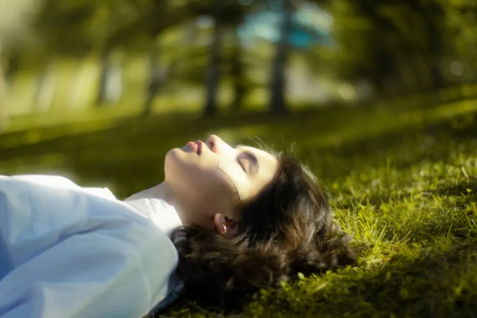 A serene portrait of a woman lying down on grass, eyes closed and relaxed in nature.